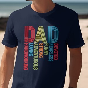 May include: Navy blue t-shirt with the word "DAD" in a retro font, with the words "hardworking, loving, adventurous, strong, funny, fearless, devoted" in a vertical column. The text is in red, yellow, blue, and green.