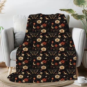 May include: A black throw blanket with a repeating pattern of gold butterflies, white flowers, and crescent moons on a dark background.
