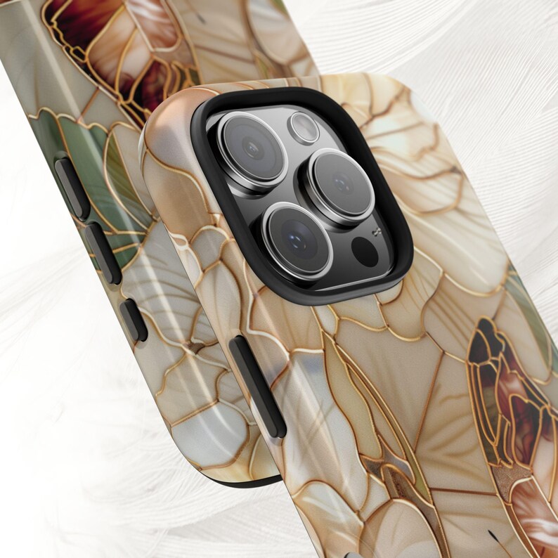May include: Close-up of two phone cases with a floral design. The cases feature a mosaic-like pattern in shades of beige, brown, and gold, with a black camera lens border. The design resembles stained glass.