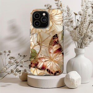 May include: A phone case with a stained glass design featuring a butterfly and flowers in shades of brown, cream, and gold. The case has a glossy finish and a raised camera bump.