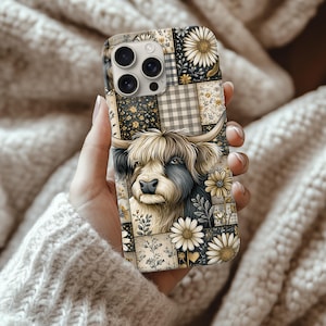 Puede incluir: Una funda de teléfono con un diseño de patchwork y una ilustración de una vaca de las Tierras Altas. La funda tiene patrones florales, de cuadros y lisos en tonos beige, negro y amarillo. La vaca tiene pelo largo y lanudo y cuernos prominentes.