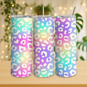 May include: Three stainless steel tumblers with lids and straws. Each tumbler features a vibrant, iridescent background with a white leopard print pattern. The colors transition from blue to purple to pink, creating a colorful and eye-catching design.