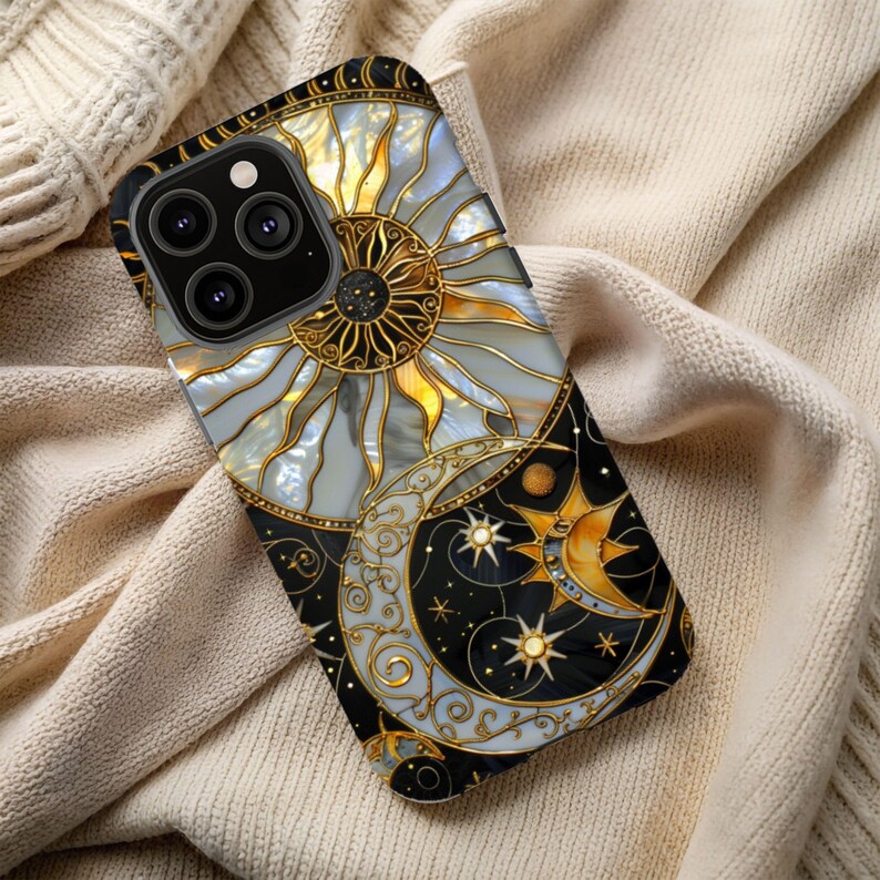 May include: A decorative phone case featuring a celestial design. The case showcases a sun and moon motif with gold and pearl accents against a black background. The design includes stars and intricate detailing, creating a stylish accessory.