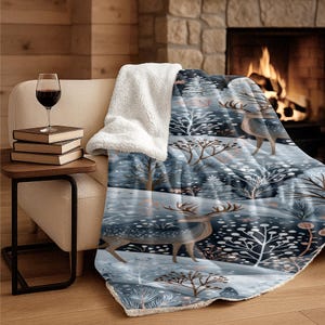 Könnte beinhalten: Eine Plüschdecke mit einer Winterwaldszene mit Hirschen, kahlen Bäumen und Schneefallmustern in Blau-, Weiß- und Brauntönen. Die Decke hat auf der Rückseite und an den Rändern ein dickes, weißes, strukturiertes Sherpa-Fleece-Futter.