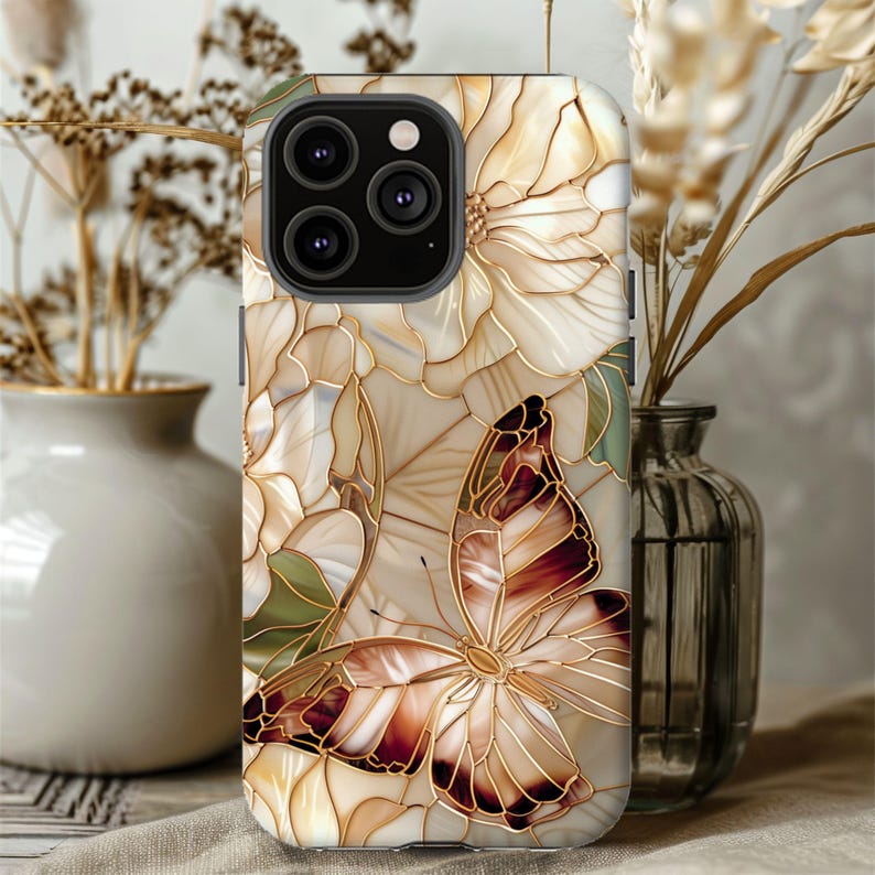 May include: A phone case featuring a butterfly and floral design. The case has a cream-colored background with gold-colored outlines. The butterfly has brown and cream-colored wings. The case is decorated with a floral pattern.