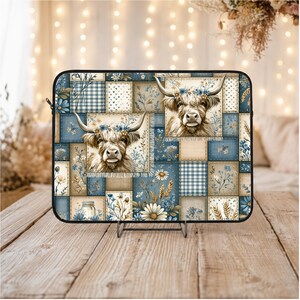 Puede incluir: Una funda para portátil con un diseño de patchwork con imágenes de vacas de las Highlands. El diseño incorpora cuadrados azules, beige y blancos con patrones florales y de cuadros. Las vacas tienen coronas de flores.