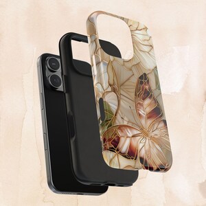 May include: A black smartphone with a protective case featuring a butterfly design. The case has a beige, brown, and gold color scheme with a butterfly and floral pattern. The case is made of a hard, durable material.