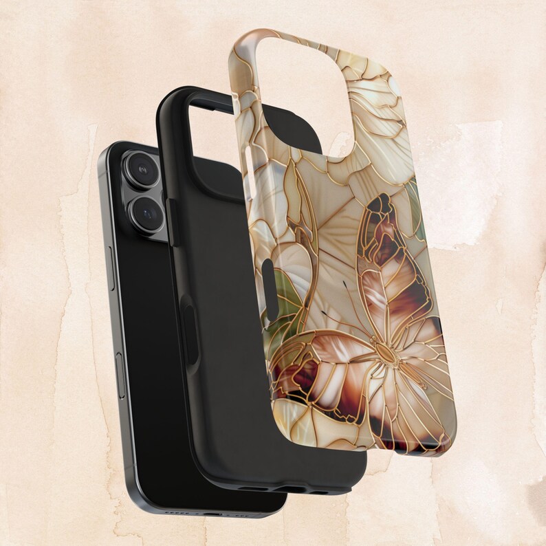 May include: A black smartphone with a protective case featuring a butterfly design. The case has a beige, brown, and gold color scheme with a butterfly and floral pattern. The case is made of a hard, durable material.
