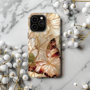 May include: A phone case featuring a butterfly and floral design. The case has a beige background with a stained glass effect. The butterfly has brown and cream-colored wings with gold outlines. The flowers are cream-colored with gold outlines.