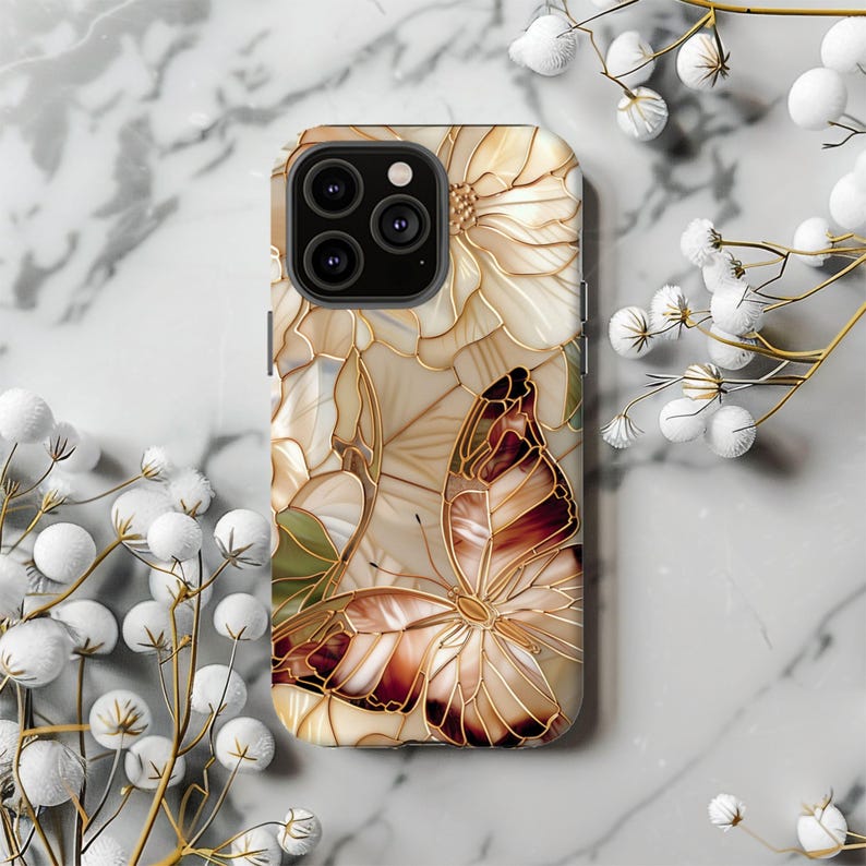 May include: A phone case featuring a butterfly and floral design. The case has a beige background with a stained glass effect. The butterfly has brown and cream-colored wings with gold outlines. The flowers are cream-colored with gold outlines.