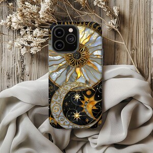 May include: A phone case featuring a celestial design with a sun and moon motif. The case has a black border and a detailed illustration of a sun with gold accents and a crescent moon with stars. The design is set against a light gray and black background.