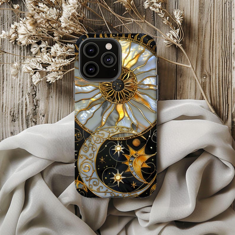 May include: A phone case featuring a celestial design with a sun and moon motif. The case has a black border and a detailed illustration of a sun with gold accents and a crescent moon with stars. The design is set against a light gray and black background.