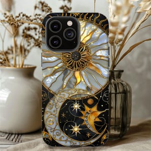 May include: A decorative phone case featuring a celestial design with a sun, moon, and stars. The case has a black background with gold and white accents. The sun and moon are intricately detailed with a stained-glass effect.