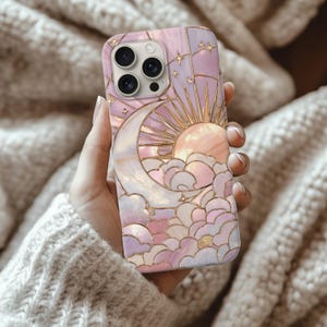 Może przedstawiać: Ozdobne etui na telefon z niebiańskim wzorem przedstawiającym słońce, księżyc, gwiazdy i chmury. Etui ma różowo-złotą kolorystykę z perłowym wykończeniem. Projekt przypomina witraż.