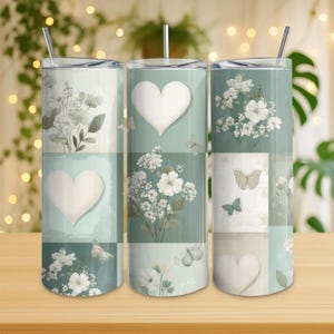 Könnte beinhalten: Drei Edelstahlbecher mit Deckeln und Strohhalmen. Jeder Becher hat ein Patchwork-Design mit Blumen- und Schmetterlingsmotiven sowie Herzformen. Die Farbpalette umfasst Grün-, Weiß- und Beigetöne.