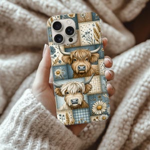 Puede incluir: Una funda de teléfono con un diseño de patchwork que presenta ilustraciones de vacas de las Highlands, margaritas y elementos florales. La funda tiene una combinación de colores azul, beige y blanco. La funda está en la mano de una persona.