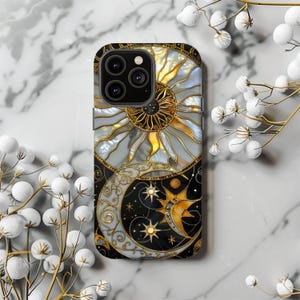 May include: A decorative phone case featuring a celestial design. The case showcases a sun and moon motif with gold accents, set against a black and white background. The sun is golden with white rays, and the moon is a crescent shape with stars.