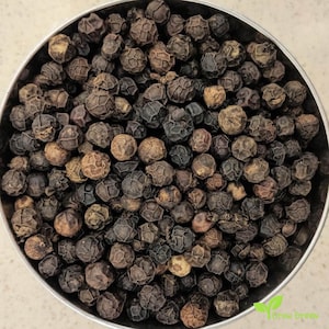 May include: A close-up image of a bowl filled with black peppercorns. The peppercorns are small and round, with a slightly wrinkled surface. They are a dark brown colour, with some appearing almost black.
