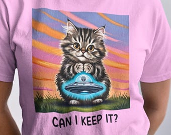 May include: A pink t-shirt with a cartoon image of a cat holding a blue flying saucer. The text "Can I Keep It?" is printed below the image.