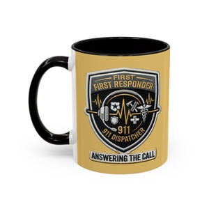 Könnte beinhalten: Ein gelber Keramikbecher mit schwarzem Henkel und schwarzem Innenraum. Die Vorderseite zeigt ein schildförmiges Emblem mit dem Text FIRST FIRST RESPONDER 911 DISPATCHER ANSWERING THE CALL sowie Symbole für Headset, Abzeichen, Axt, Leiter und Äskulapstab.
