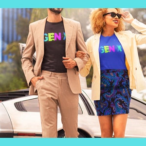 May include: Two people wearing t-shirts with the text "GEN X" in rainbow colors. The person on the left is wearing a black t-shirt and a beige blazer. The person on the right is wearing a blue t-shirt and a white blazer. They are standing in front of a silver car.