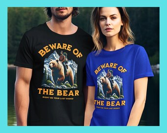 May include: Black and blue t-shirts with the text "BEWARE OF THE BEAR" and an illustration of a person riding a bear. The graphic also includes the text "MIGHT BE YOUR LAST RODEO". The shirts are displayed on two people.