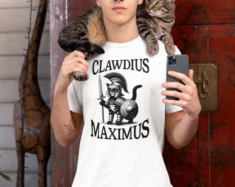 May include: White t-shirt with a black and white illustration of a cat dressed as a Roman soldier. The text "CLAUDIUS MAXIMUS" is printed on the shirt.