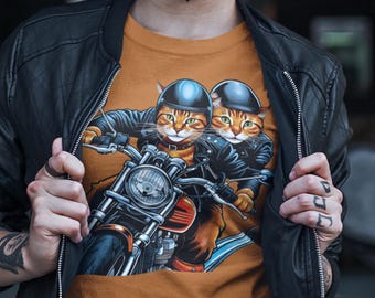 May include: A brown t-shirt with a graphic of two cats wearing helmets and riding a motorcycle. The cats are wearing leather jackets and the motorcycle has a chrome headlight.