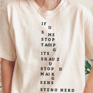 Peut inclure: T-shirt ivoire avec texte noir. Le texte se lit : "IF U S ME STOP TAOI P G ITS SKAU Z U STOP D MAIK G SENS STENO NERD." Le t-shirt est de taille large.