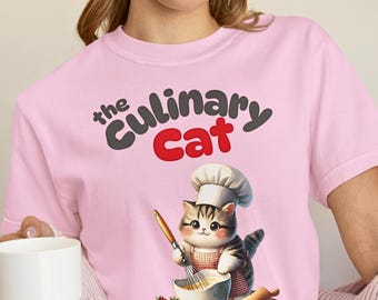 May include: Pink t-shirt featuring the text "the Culinary Cat" above an illustration of a cat wearing a chef's hat and apron, whisking ingredients in a bowl. A wooden cutting board with strawberries and a rolling pin is also shown.