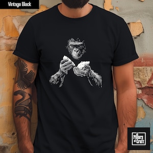 May include: Black t-shirt with a detailed white illustration of a chimpanzee holding two rocks. The text "Vintage Black" is at the top left. The shirt is from "Pillars of Craft".