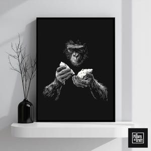 May include: Black and white framed art print featuring a detailed illustration of a gorilla holding two pieces of rock. The artwork is set against a solid black background. The print is displayed on a white shelf with a black vase and decorative branches.