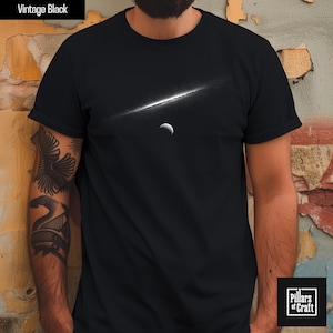 May include: Black t-shirt with a white graphic of a celestial scene featuring a bright diagonal line and a crescent moon. The words "Vintage Black" are at the top left. The Pillars of Craft logo is at the bottom right.
