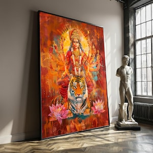 Op de afbeelding: Groot ingelijst kunstwerk met een veelarmige godheid op een tijger. Het kunstwerk gebruikt levendige kleuren, waaronder rood, oranje en geel, met lotusbloemen aan de onderkant. Het kunstwerk wordt tentoongesteld in een kamer met een standbeeld en een raam.