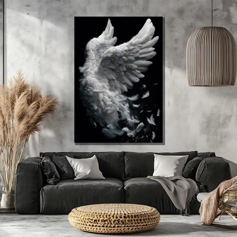 May include: A large framed canvas art print featuring a white angel wing against a black background. The wing is detailed with individual feathers, some of which appear to be floating away. The artwork is displayed above a dark gray sofa in a modern living room setting.