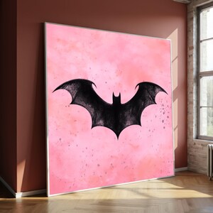 May include: A framed artwork featuring a black bat silhouette against a pink watercolor background. The bat has outstretched wings, and the pink background has subtle darker pink splatters. The artwork is displayed in a room with a window.
