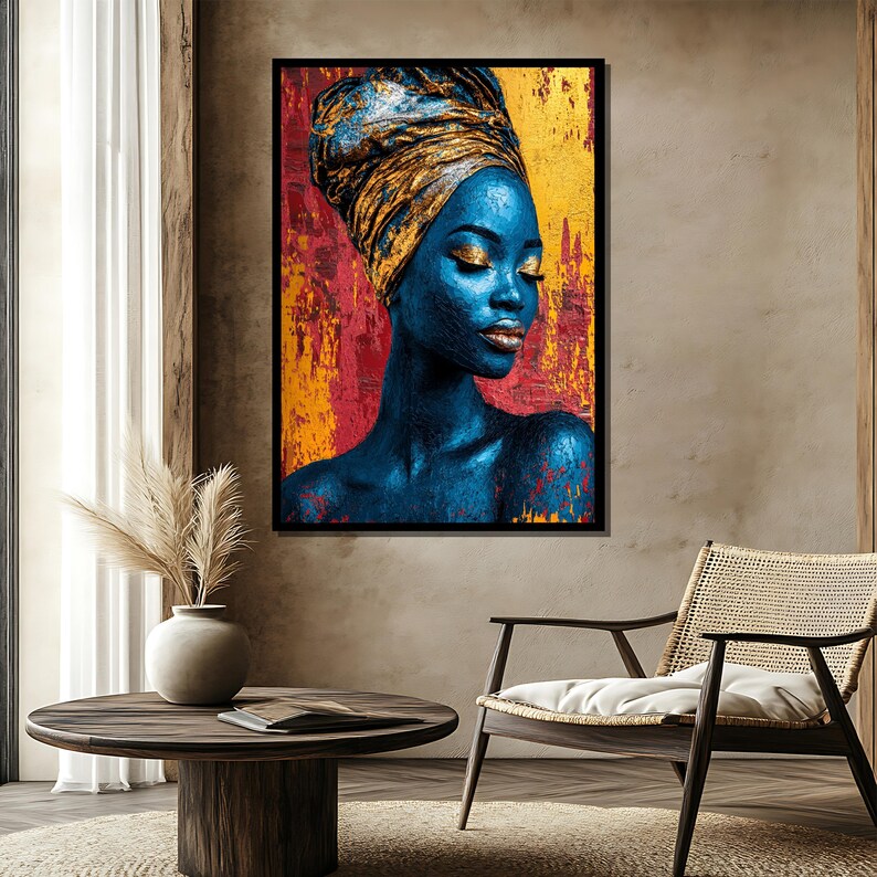 May include: A framed art print featuring a portrait of a person with blue skin and gold makeup, wearing a gold head wrap. The background is a textured mix of red, yellow, and gold. The artwork is displayed in a room with a round wooden table and a woven chair.