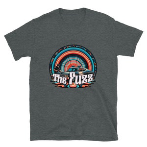 May include: A dark heather grey t-shirt with a retro-style graphic of a police car and the text "The Fuzz" in a colorful, psychedelic font.