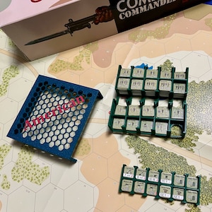 Puede incluir: Una bandeja de plástico azul con un patrón de panal y la palabra "American" impresa en rosa. La bandeja se utiliza para guardar y organizar pequeñas piezas de juego. Las piezas de juego están en dos filas de contenedores de plástico con números impresos en ellos. Los contenedores están etiquetados con números y texto como "Light MG", "Medium MG", "Radio" y "111-121".