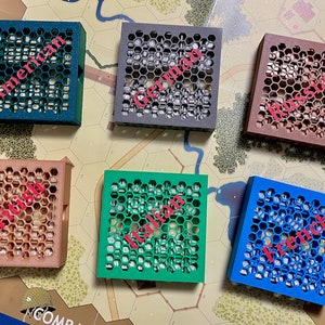 Peut inclure: Six petites boîtes carrées imprimées en 3D avec un motif en nid d'abeille. Chaque boîte est d'une couleur différente et porte une nationalité différente imprimée en rose : américaine, allemande, russe, britannique, italienne et française.