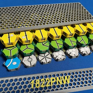 May include: A collection of colorful, geometric game pieces, including yellow, green, blue, and gray hexagonal tiles, are arranged in a gray storage container. The text "1822PNW" is visible in yellow on a matching gray piece.