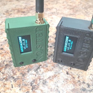 May include: Two small, rectangular electronic devices, one green and one black, with small screens displaying "MESHCORE v1.11.0". Each has an antenna and the text "NO STEP" on the side.