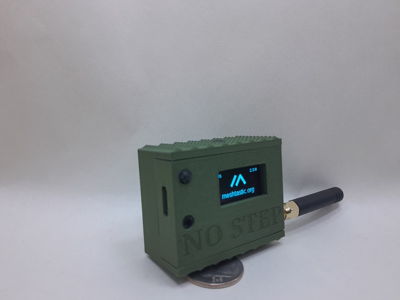 May include: A small, green, rectangular device with a black antenna and a screen displaying a blue arrow and the text "meshtactic.org". The device has the text "NO STEP" printed on the front.