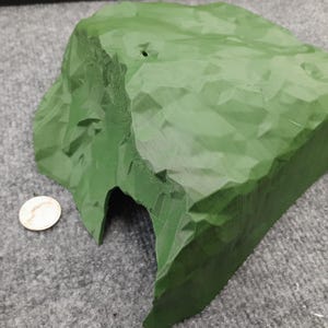 Pode incluir: Uma rocha verde, impressa em 3D, texturizada com uma abertura de caverna. A rocha &eacute; projetada para uso em layouts de trens em miniatura ou outras cenas em miniatura.