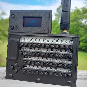 May include: A black, handheld device with a small screen displaying the text "remarkable.io". The device has a keyboard with keys labeled with letters, numbers, and symbols. The device has a black antenna.