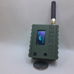 May include: A green, rectangular device with a small screen displaying "mesh.asic.org" and a signal strength indicator. The device has a black antenna and the text "Mini-STRD" printed on the side.