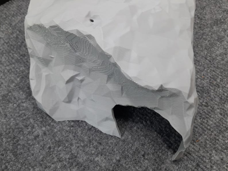May include: A white 3D printed rock with a cave opening. The rock has a textured surface and appears to be made of plaster or resin.