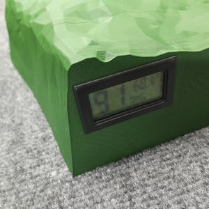 Pode incluir: Uma caixa retangular verde texturizada com um visor digital preto mostrando o n&uacute;mero "91".