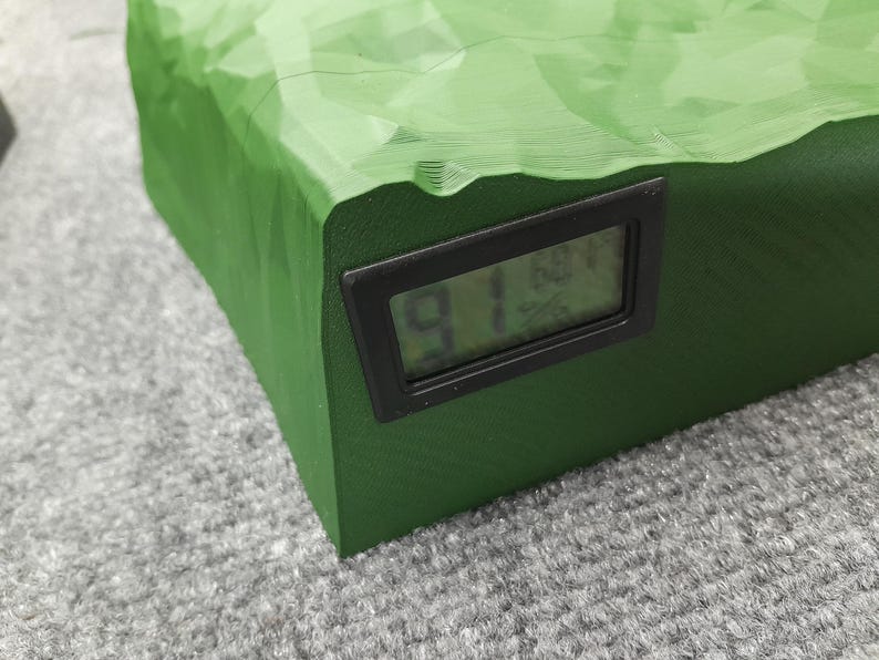 Pode incluir: Uma caixa retangular verde texturizada com um visor digital preto mostrando o n&uacute;mero "91".