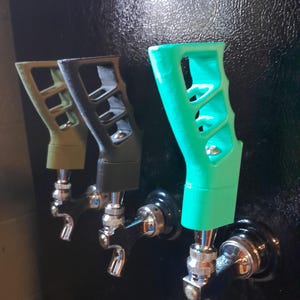 May include: Three beer tap handles with different colored grips. The handles are black with a silver tap. The grips are green, black, and turquoise.